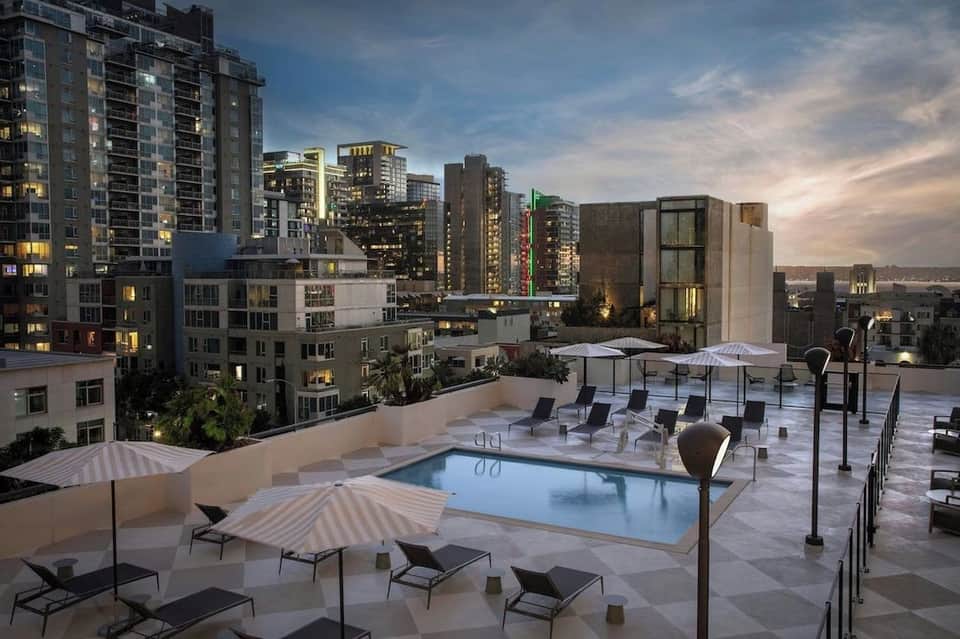 Elevated pool terrace at night with umbrellas, loungers, and illuminated city views