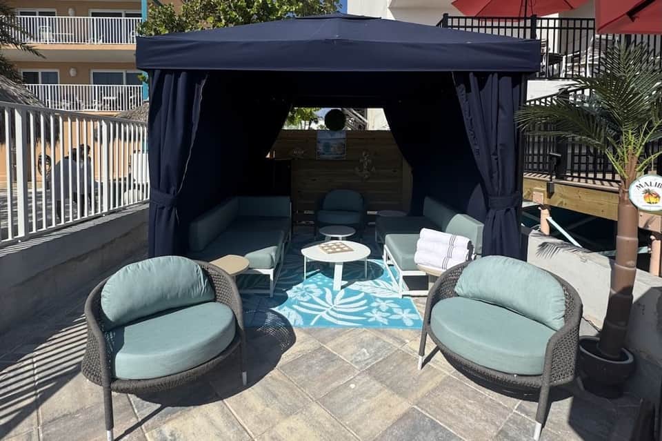 Outdoor cabana with dark navy curtains, mint green seating, and turquoise patterned rug