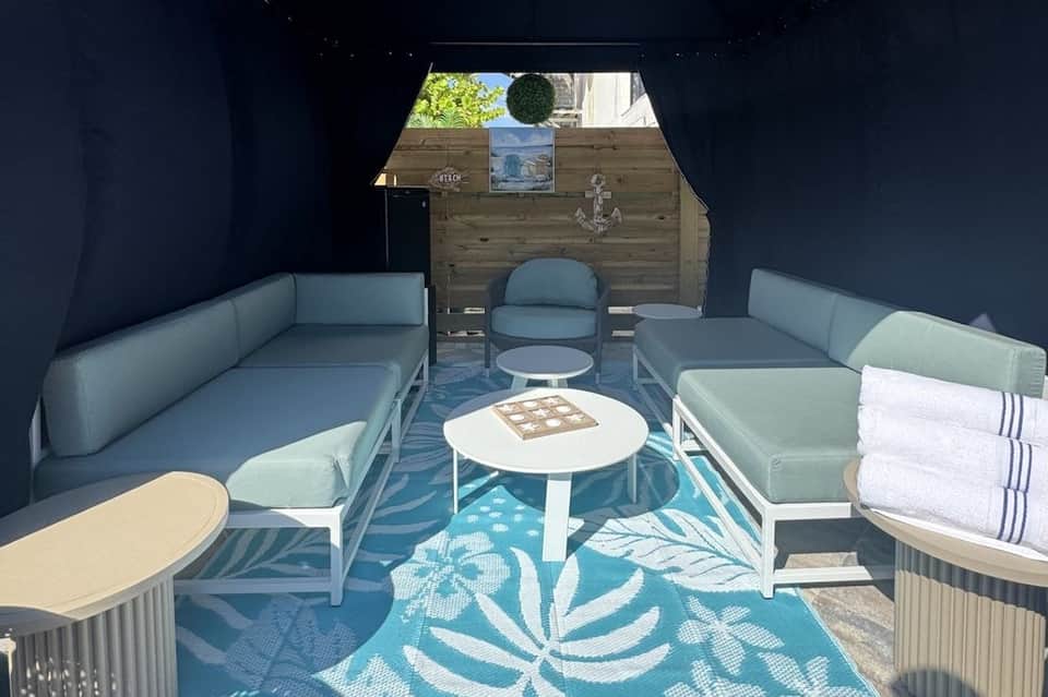 Interior of dark blue cabana with light blue seating, white tables, and wooden back wall
