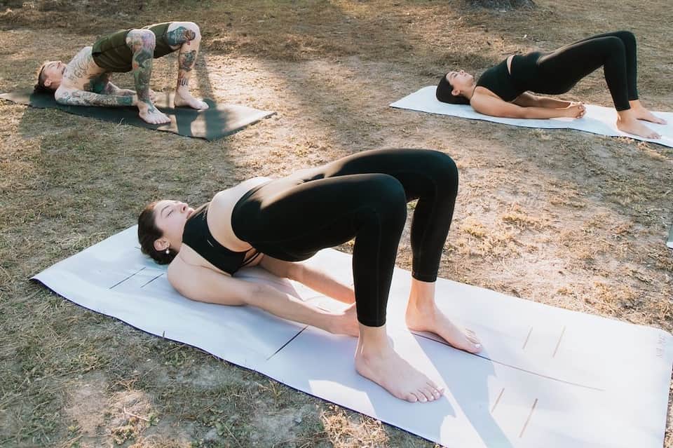 Outdoor yoga class with three people performing exercises on white mats on dirt ground