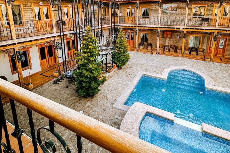 Courtyard with two blue pools, wooden balconies, and brick architecture surrounding paved area