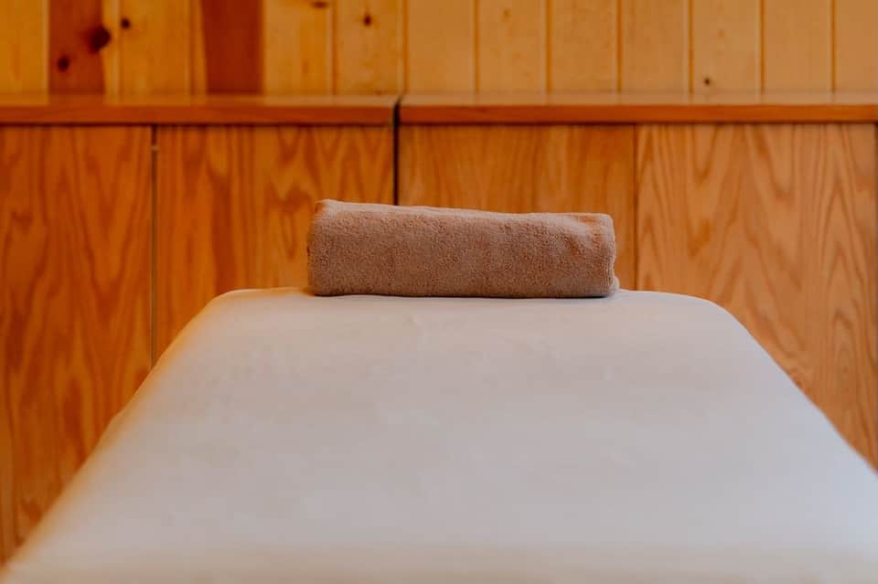 Rolled brown towel on white bed pillow against wooden wall paneling