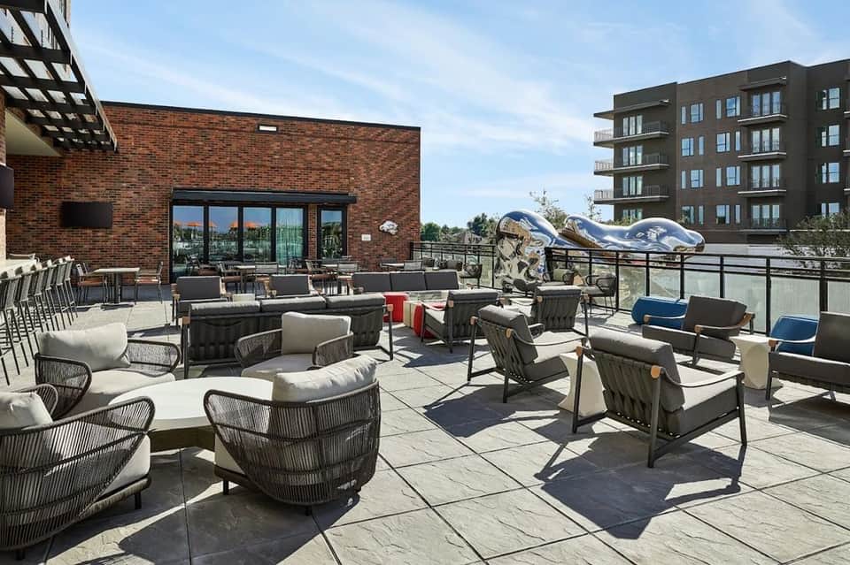 Rooftop terrace with wicker lounge chairs, fire pit, brick building, and modern apartment complex in background