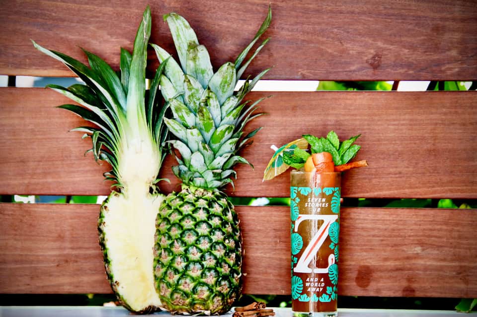 Sliced pineapple and tropical beverage on wooden deck railing with ocean view background