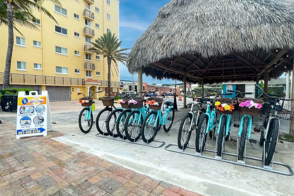 Turquoise bikes parked under thatched shelter with yellow building and palm trees in background