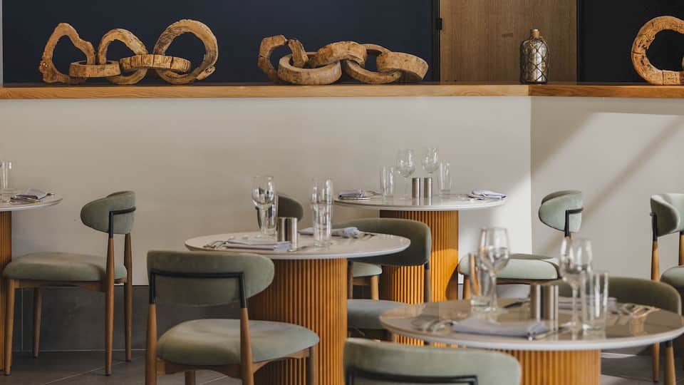 Modern fine dining restaurant interior with round tables, sage chairs, and decorative wooden wall accents