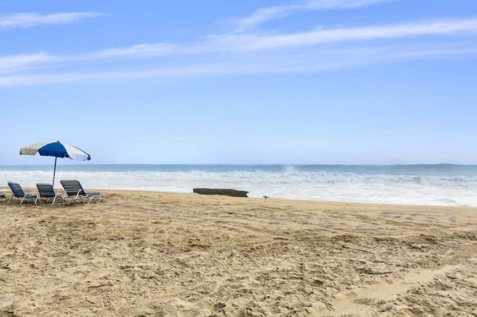 Beach setup with blue and tan umbrella shading lounge chairs facing the ocean