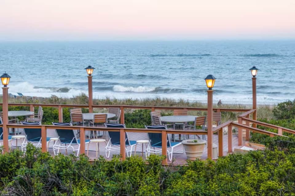 Elevated wooden deck with lounge chairs overlooking beach and ocean at dusk
