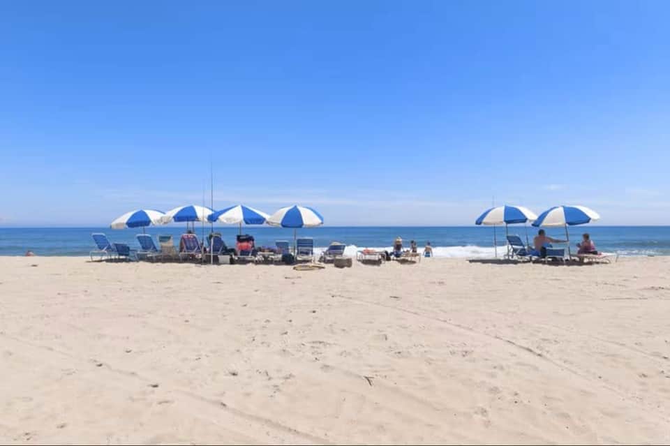 Beach scene with multiple blue and white umbrellas, lounge chairs, and beachgoers