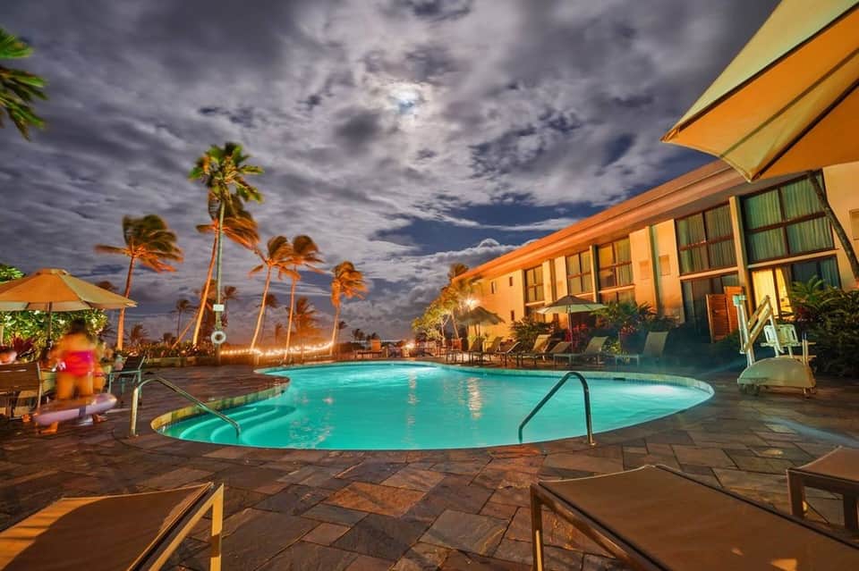 Resort pool at dusk illuminated by warm lighting, surrounded by palm trees and modern building architecture