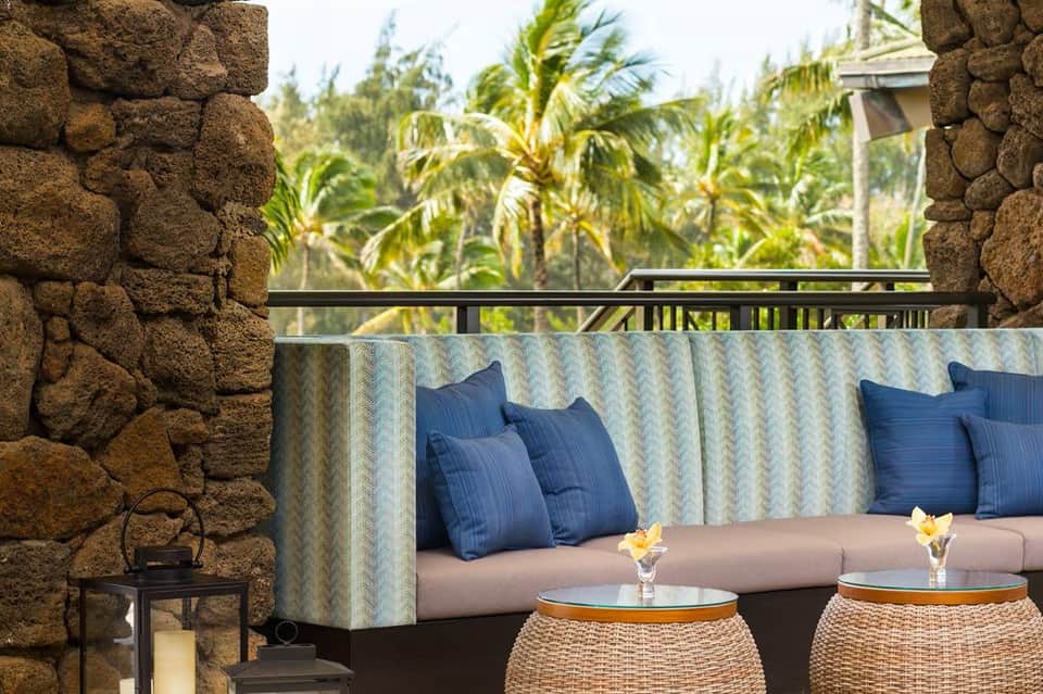 Outdoor lounge seating on stone terrace with cushioned sofa, blue pillows, tropical vegetation, and palm trees