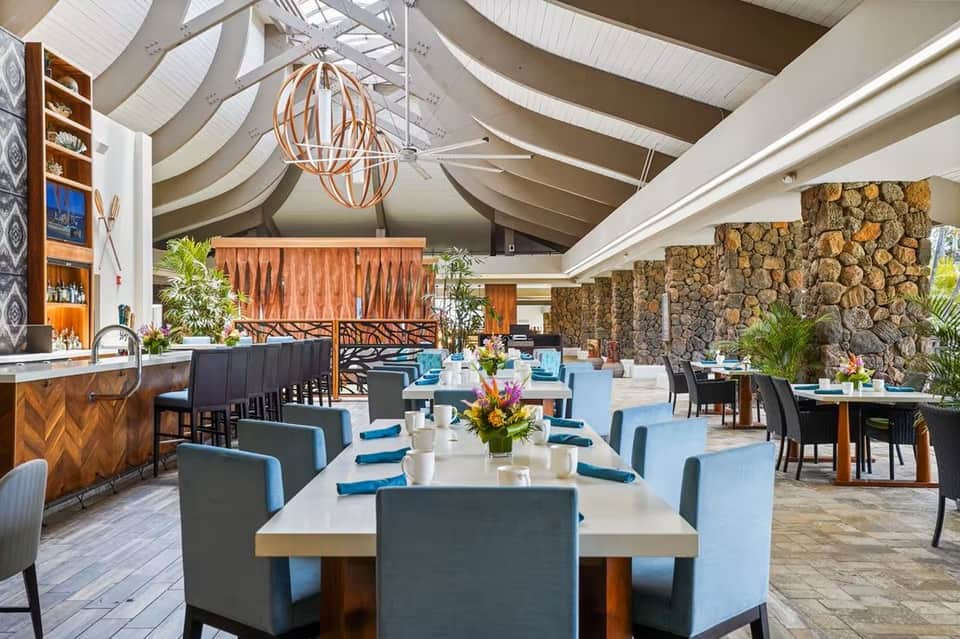 Elegant dining hall with curved white ceiling, hanging globe lights, stone fireplace, and blue-upholstered seating