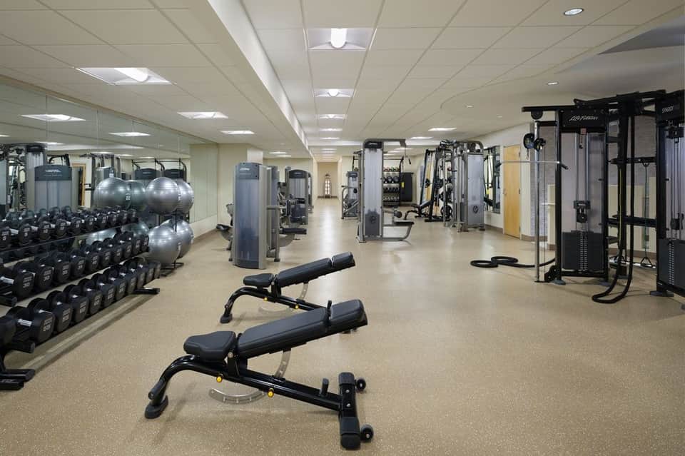 Spacious gym with dumbbells, weight machines, stability balls, and mirrored walls for strength training