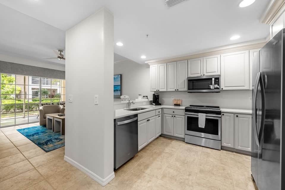 Modern kitchen with white cabinetry, stainless steel appliances, and view to screened patio and grounds