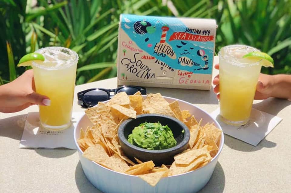 Tropical beachside setting with two margaritas, guacamole and chips, and Sea Islands travel map on table