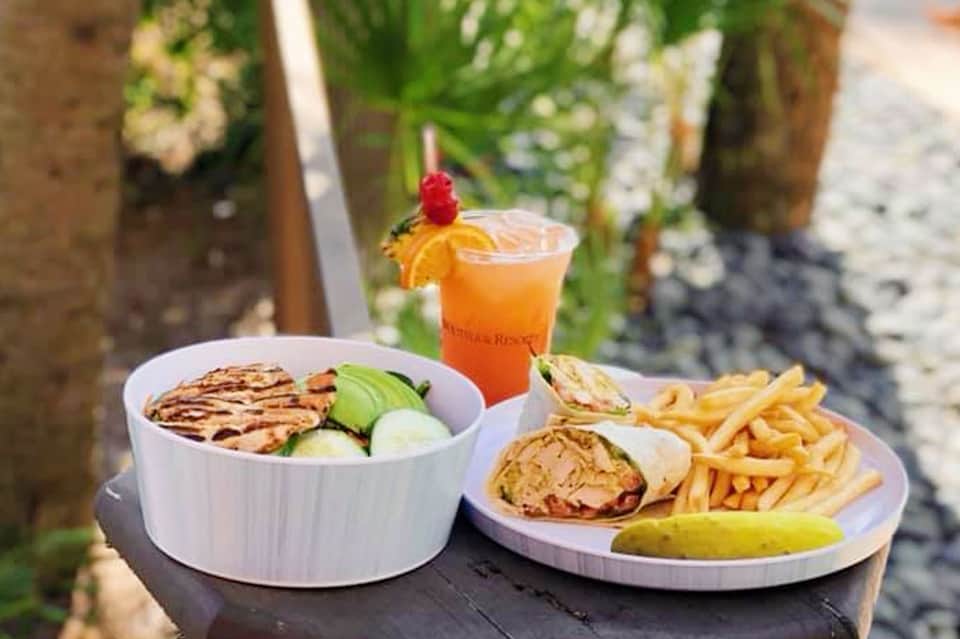 Beachside meal with grilled fish bowl, sandwich, fries, and orange cocktail