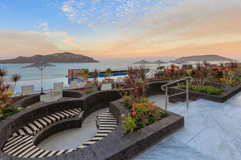 Luxury terrace with curved seating, tropical plants, and infinity pool overlooking islands at sunset