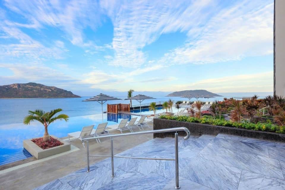 Beachfront resort deck with loungers, umbrellas, and panoramic ocean views of distant islands