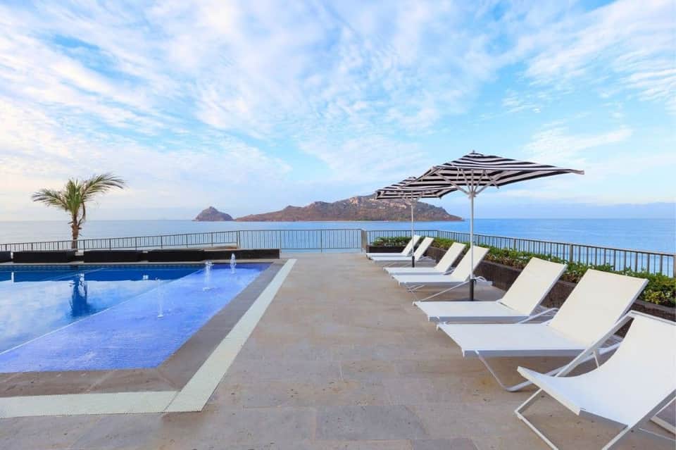 Rooftop pool deck with loungers, striped umbrella, and dramatic coastal mountain views
