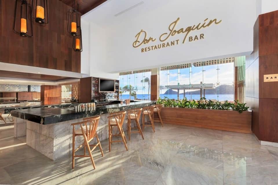 Modern restaurant interior with wood accents, black marble bar, pendant lighting, and panoramic sea views through floor-to-ceiling windows