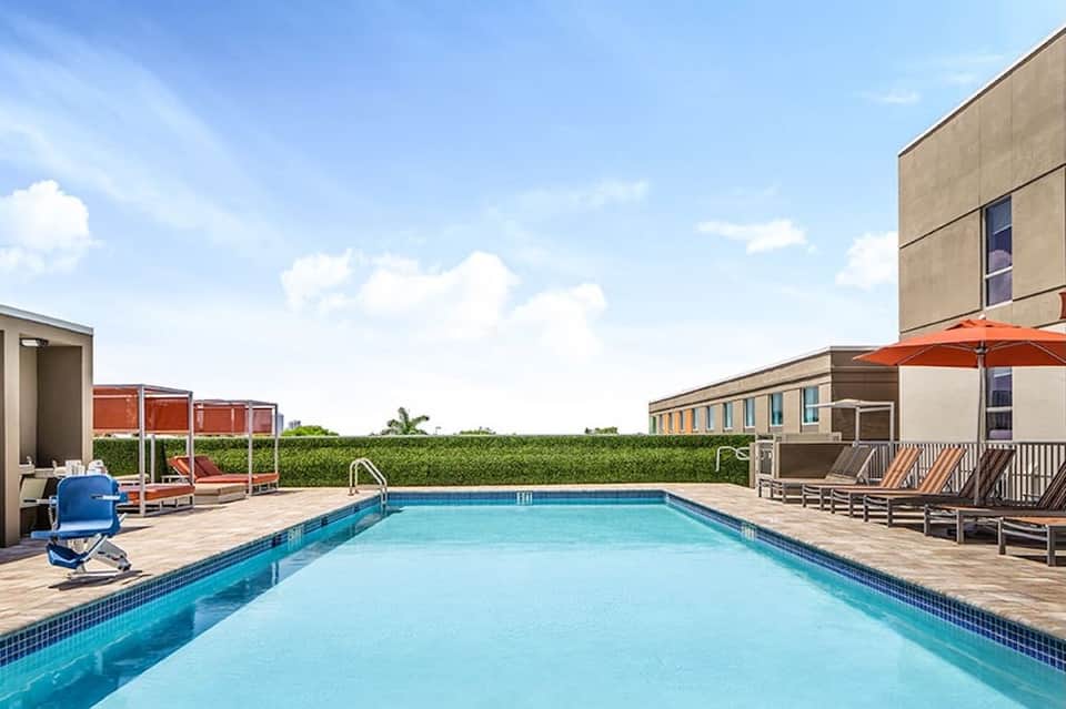 Outdoor swimming pool with lounge chairs, umbrellas, and modern hotel building under blue sky