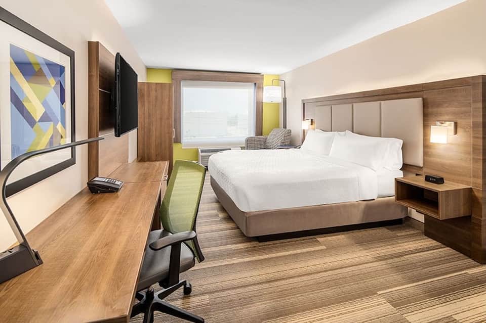 Modern hotel bedroom with queen bed, work desk, flat-screen TV, and green accent wall