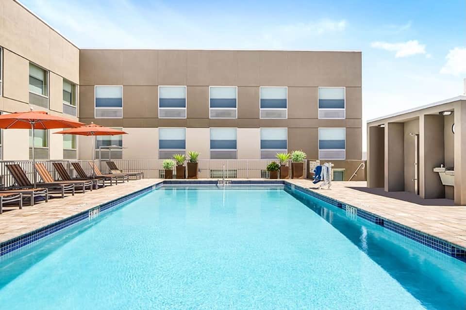 Resort outdoor pool with lounge chairs and orange umbrellas, modern building with grid windows in background
