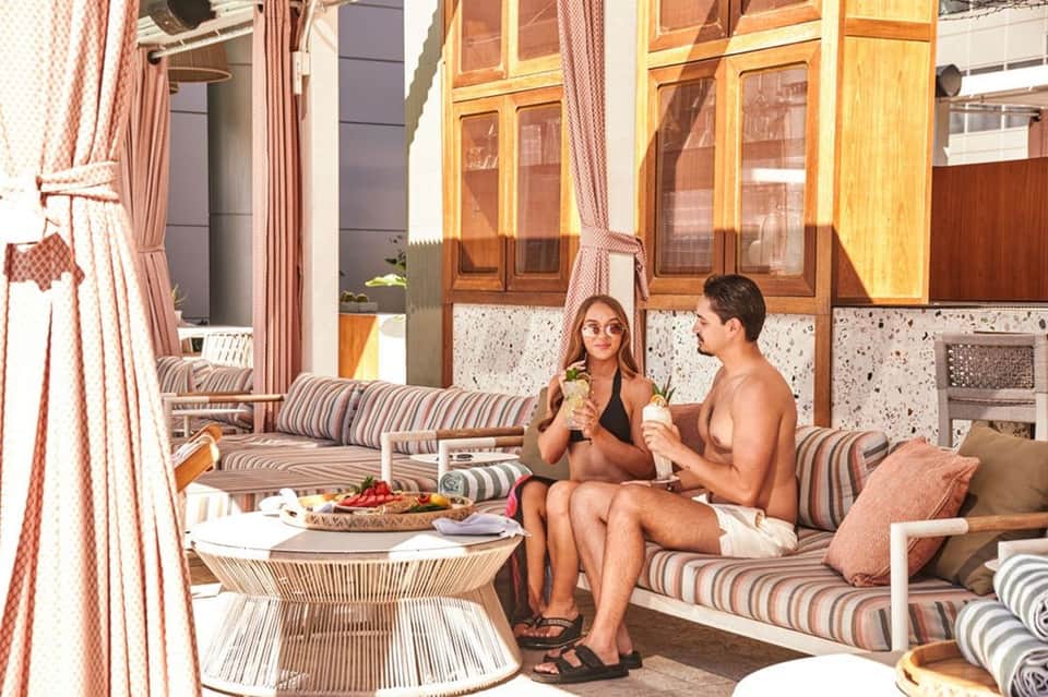 Couple relaxing on striped seating with tropical drinks and fruit platter on a terrace