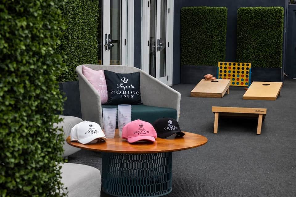 Outdoor lounge area with gray chair, wooden table, cornhole boards, and black ivy hedge wall