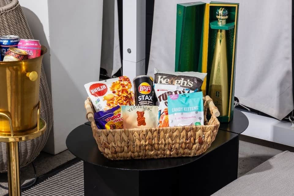 Woven basket filled with snacks, chips, candy, and premium spirits bottles on dark table