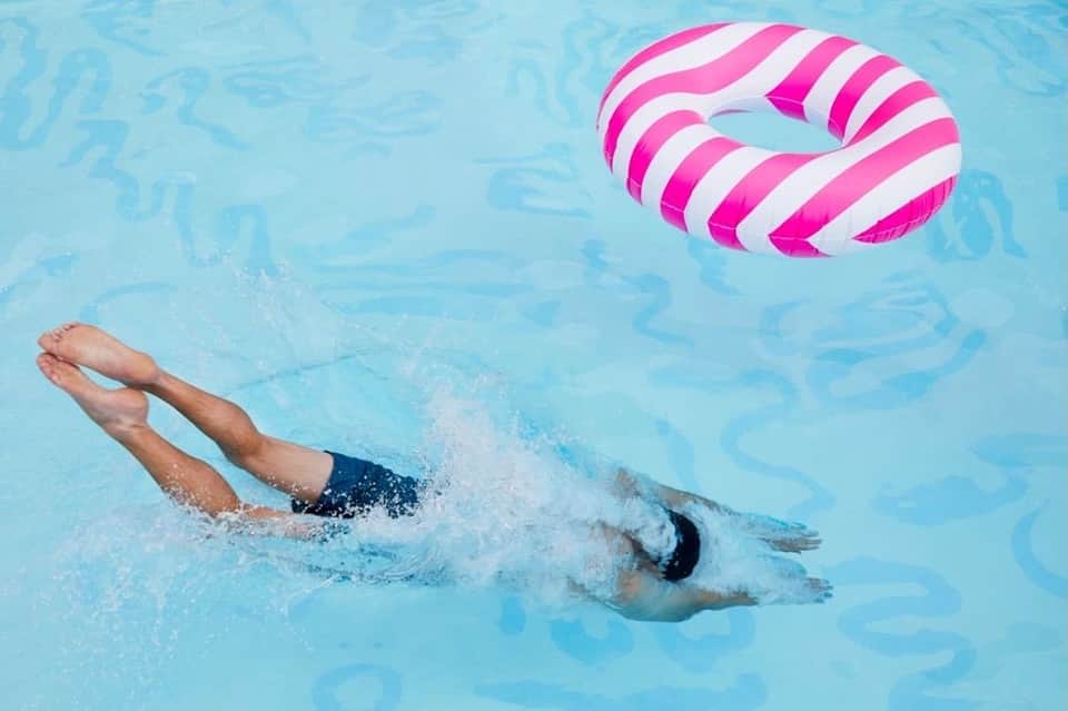 Swimmer doing freestyle stroke in pool with pink and white striped inflatable float nearby