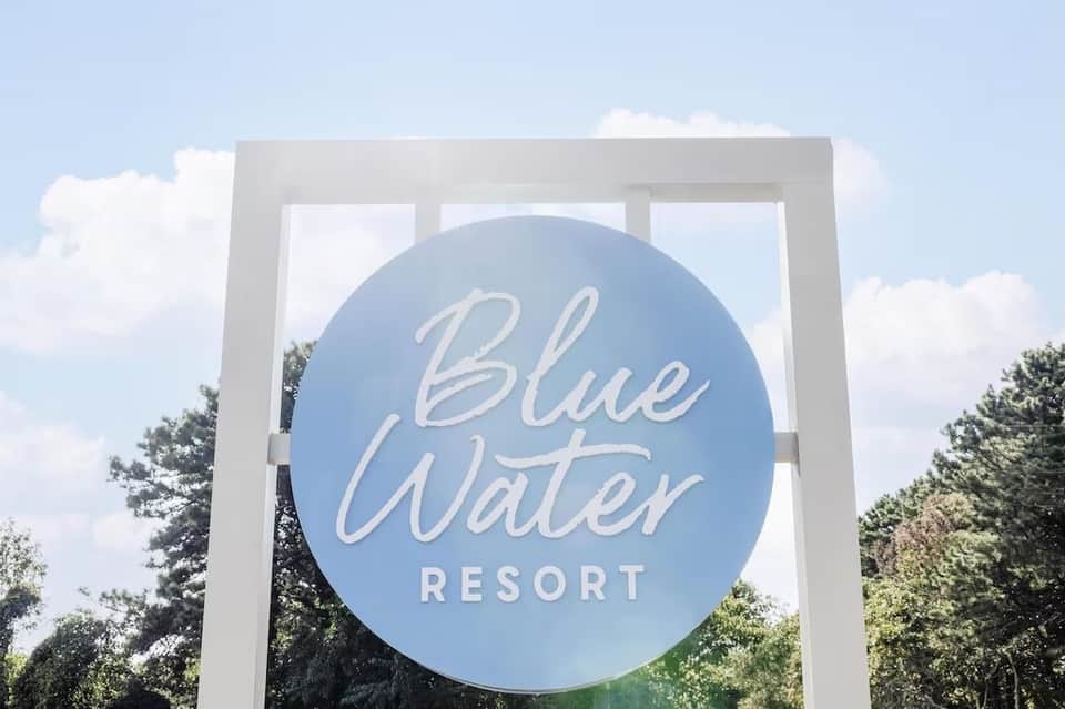 Blue Water Resort entrance sign with white frame against cloudy sky and green trees