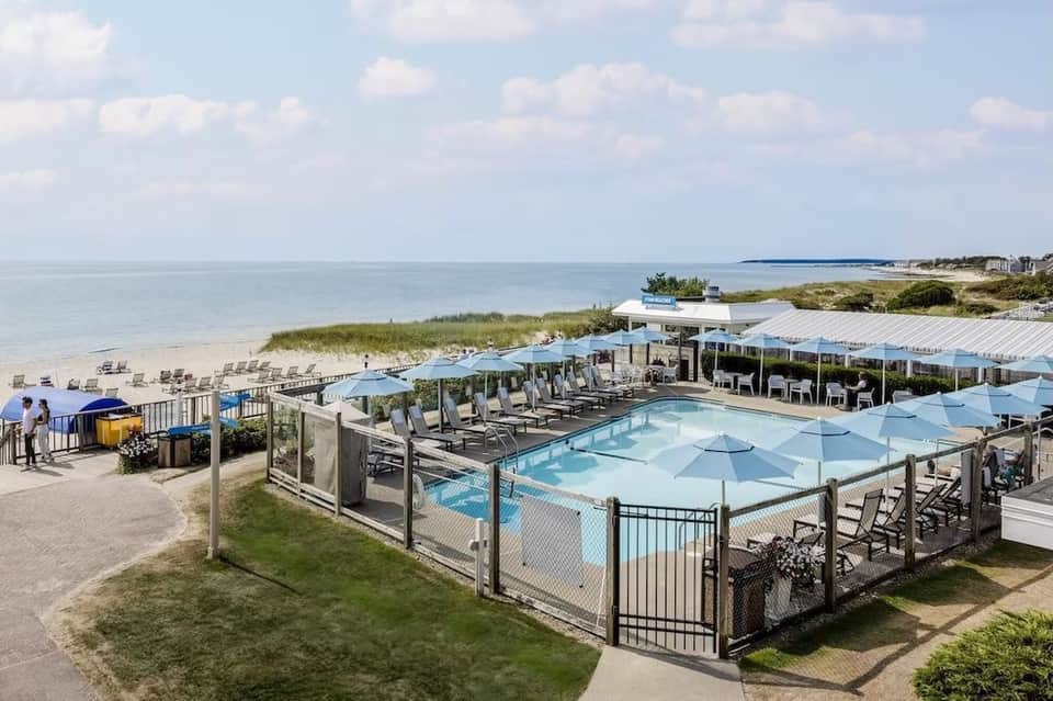 Aerial view of beachfront resort with outdoor pool, umbrellas, and ocean access along sandy shore