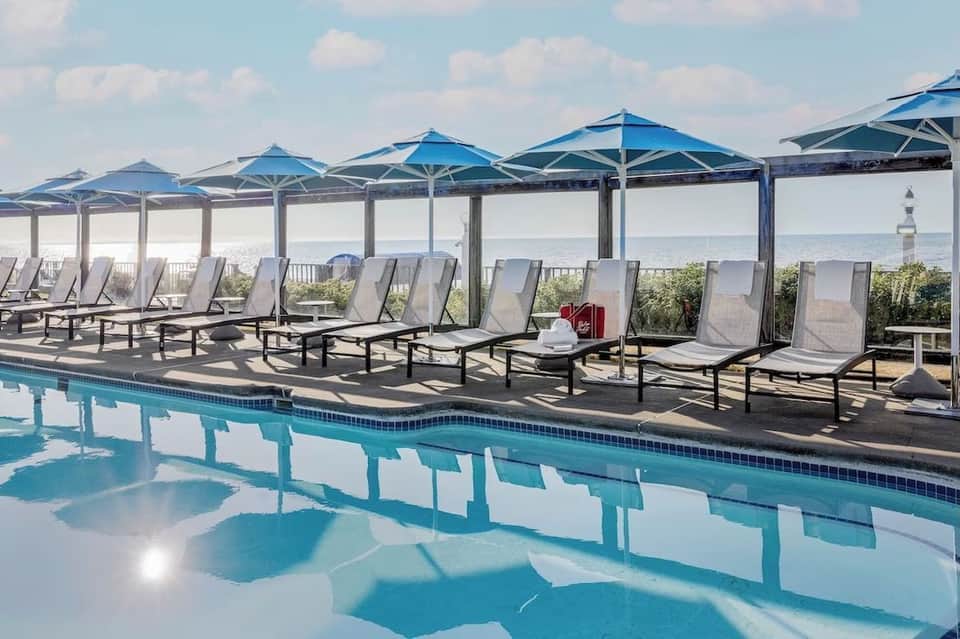 Resort pool deck with blue umbrellas, lounge chairs, and panoramic ocean horizon view