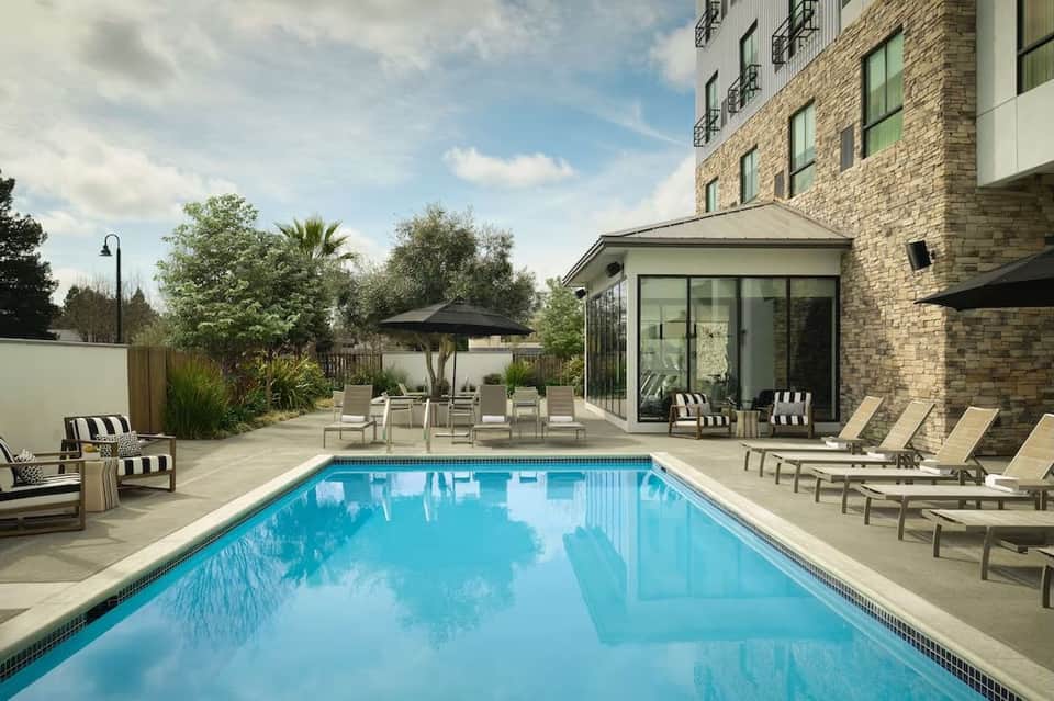 Resort swimming pool with crystal blue water, loungers, umbrellas, and brick building with patio seating area