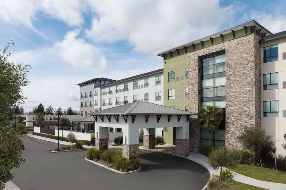 Hotel exterior entrance with modern architecture, mixed stone and brick facade, covered porte-cochere, and landscaping