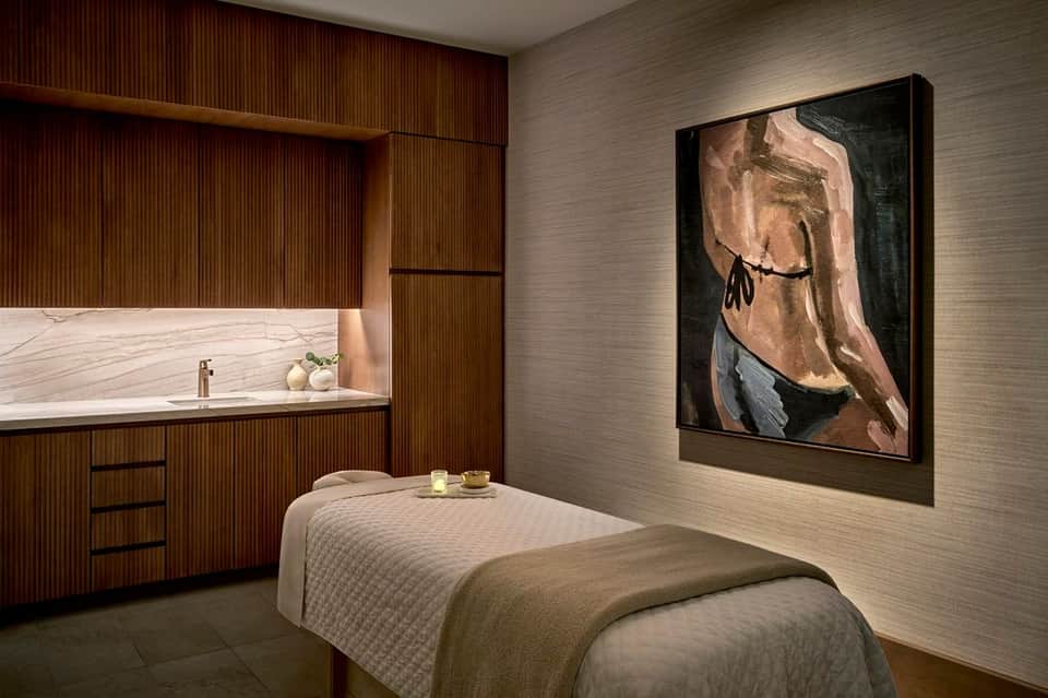 Individual spa treatment room with massage bed, wooden cabinetry, sink, and artistic wall display