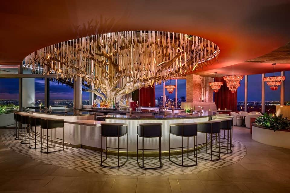 Luxury rooftop bar with dramatic chandelier, curved counter seating, and cityscape views at dusk
