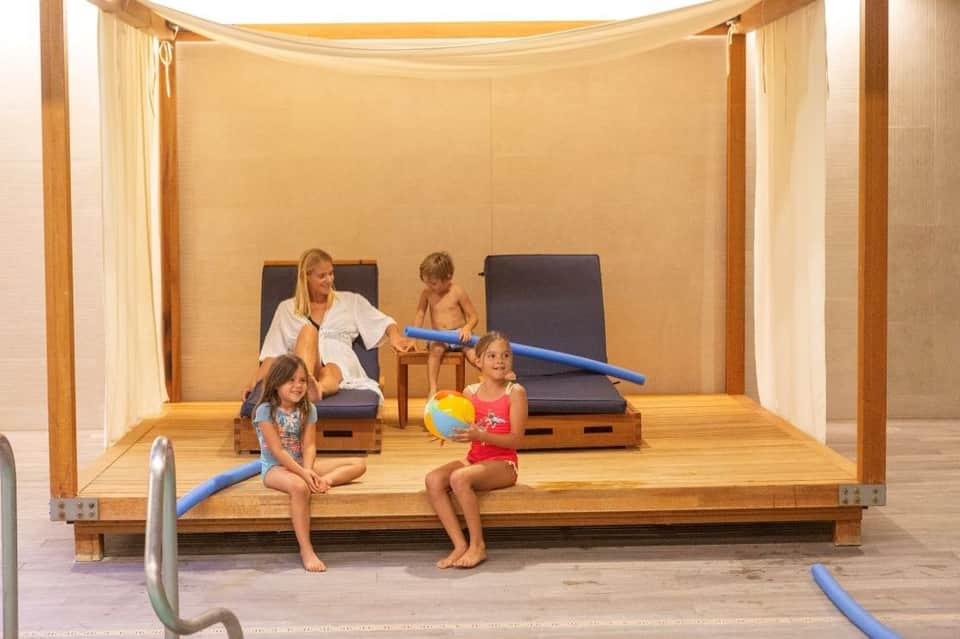 Kids' activity room with instructor, children playing with foam noodles and beach ball on wooden platform