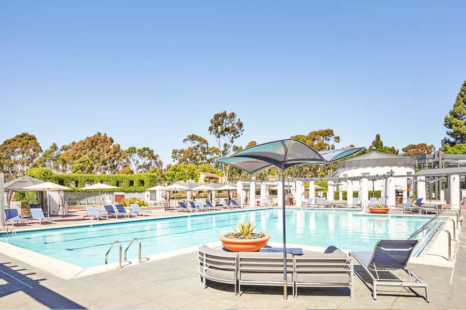 Resort pool area with lounge chairs, umbrellas, and manicured grounds under clear sky