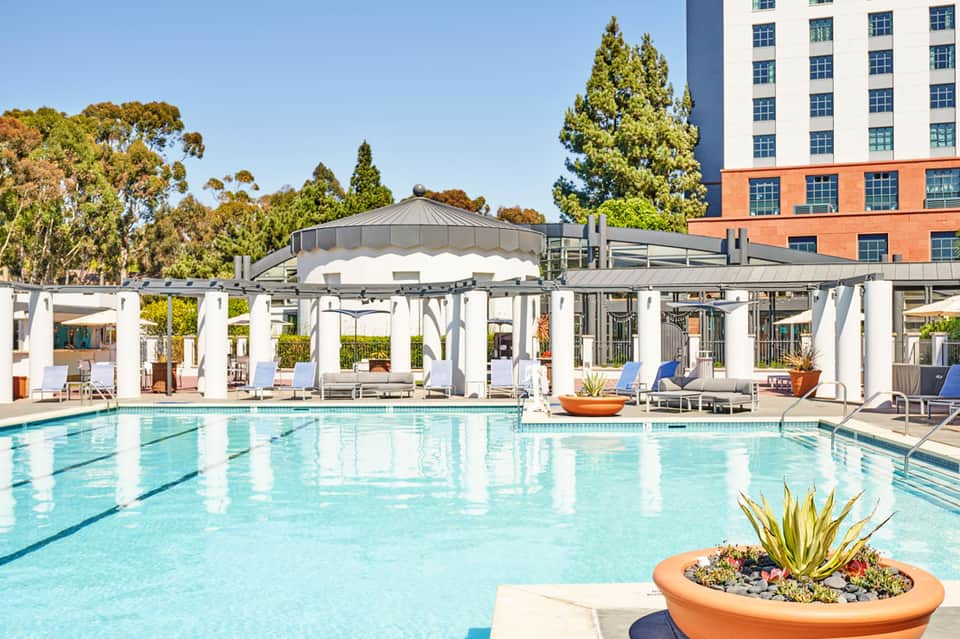 Luxury resort swimming pool with white pergolas, lounge chairs, and modern buildings in background
