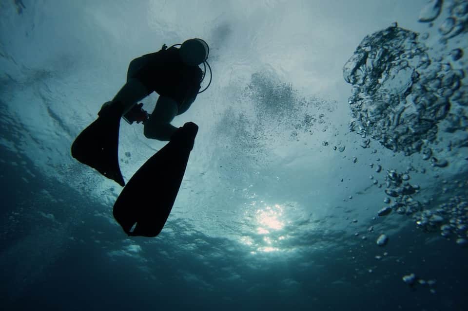 Scuba diver in silhouette exploring underwater coral reef with light filtering from surface above
