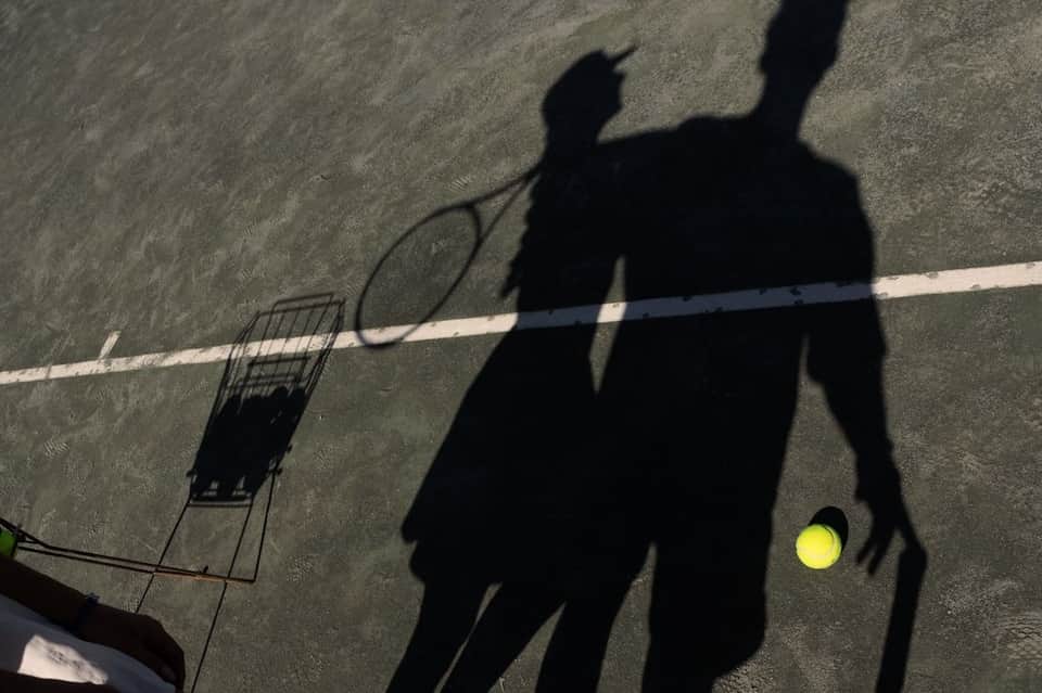 Shadow of person playing tennis with yellow ball on outdoor court