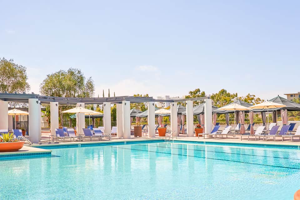 Resort pool with turquoise water, white pergolas, blue lounge chairs, and manicured landscape