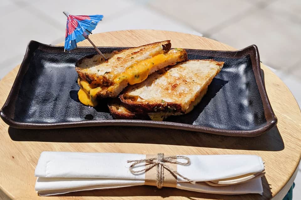 Grilled fish fillets with mango on black ceramic plate with decorative cocktail umbrella and napkins