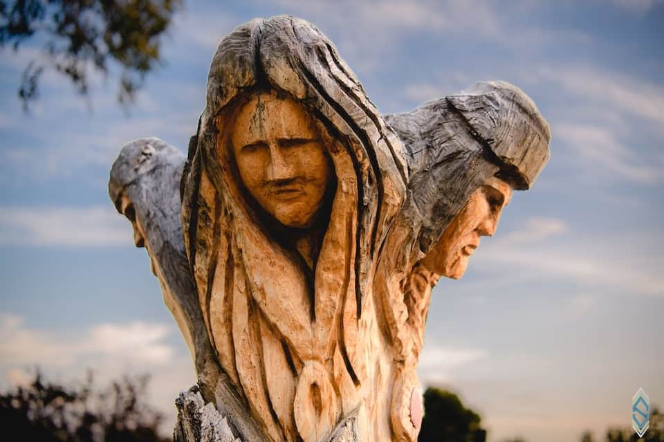 Wooden carved sculpture of three faces outdoors against cloudy sky