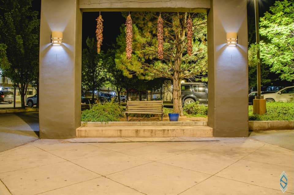 Illuminated covered pavilion with concrete bench and landscaped trees at night in resort courtyard