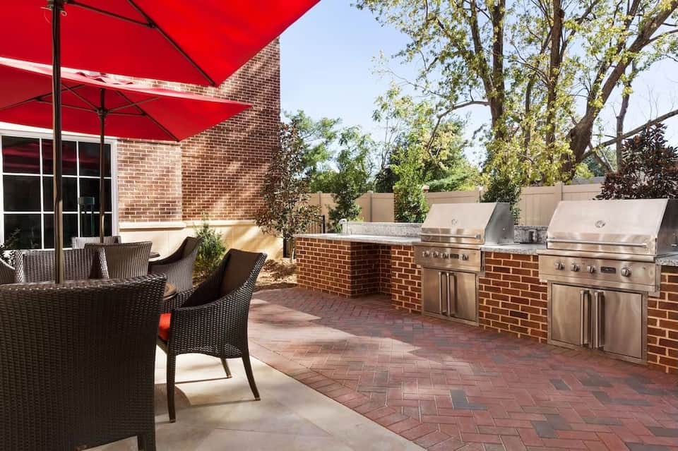 Brick patio with outdoor dining furniture, red umbrella, and built-in stainless steel grill