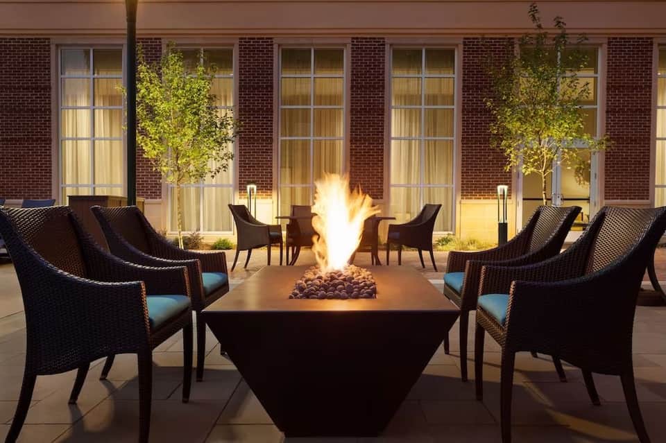 Outdoor fire pit lounge at night with wicker chairs and brick building backdrop
