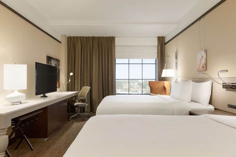 Modern hotel guest room with two queen beds, desk, and panoramic window views